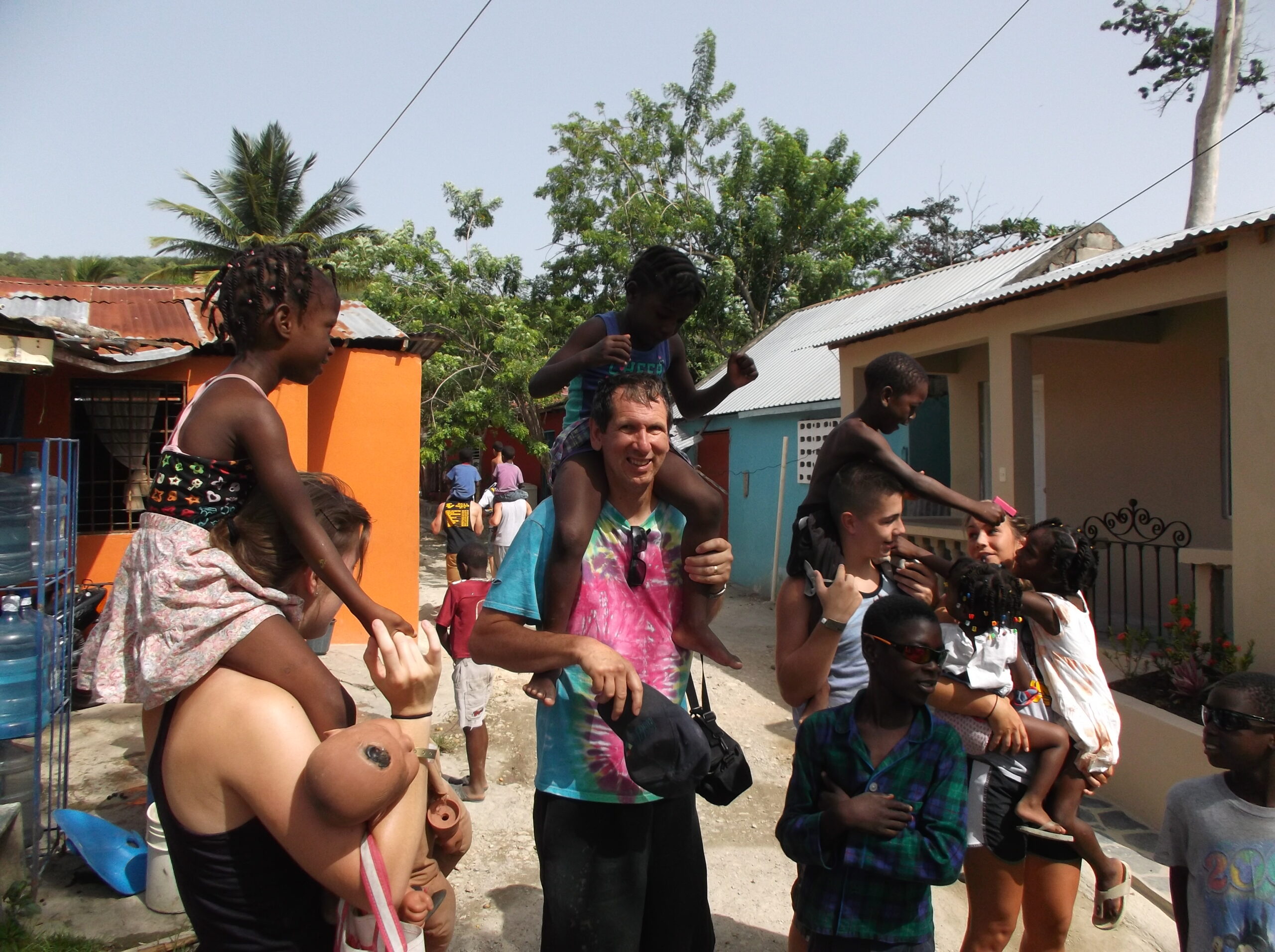 Image of Gordan Douglas carrying a little boy on his shoulder surrounded by happy kids in the Dominican Republic